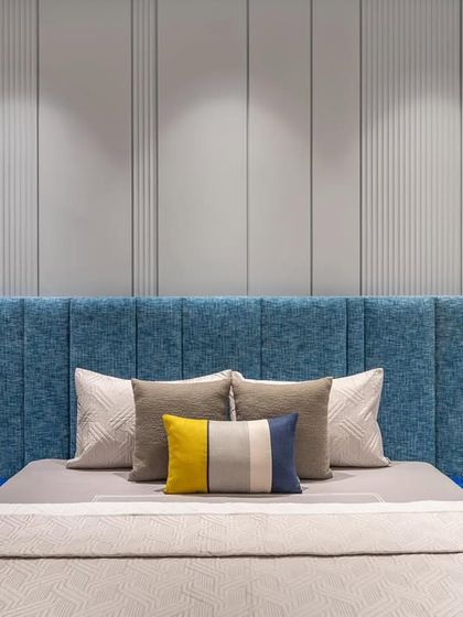 In the master bedroom, a soothing blue palette sets the tone for relaxation. The upholstered headboard is complemented by a subtle grey-paneled wall and integrated lights for a cozy atmosphere.