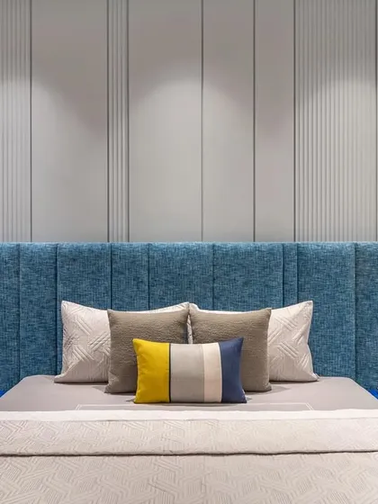 In the master bedroom, a soothing blue palette sets the tone for relaxation. The upholstered headboard is complemented by a subtle grey-paneled wall and integrated lights for a cozy atmosphere.