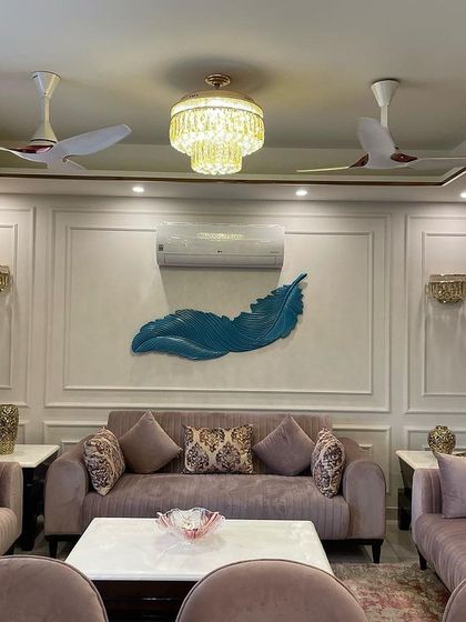 The focal point of this living room is the accent wall, featuring classic moulding and a striking blue feather art piece. The dusty rose sofas provide a soft, complementary color.