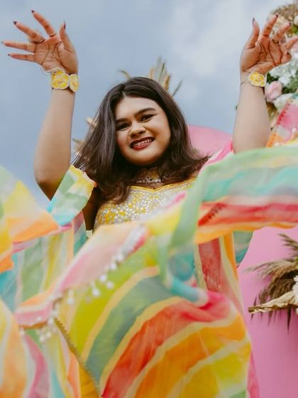 A bride in a rainbow-colored outfit dances with joy during her Mehendi or Haldi ceremony.