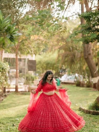 A wide shot showing how beautifully the red lehenga stands out against a natural green background. Perfect for pre-wedding photoshoots.