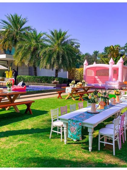 An overview of the party space, showing the poolside dining setup, lush green lawn, and a pink bouncy castle. I ensure that even the fun activities match the party's aesthetic.