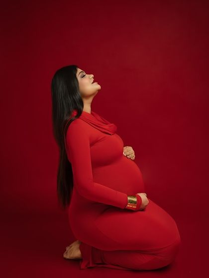 A moment of quiet reflection and strength. This kneeling pose, with the mother-to-be looking upwards, conveys a sense of hope and power. The rich red color and simple background keep the focus entirely on her.