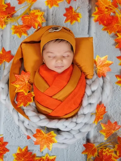 An overhead shot of a newborn wrapped in an autumn-themed swaddle, nestled in a soft basket and surrounded by colorful leaves.
