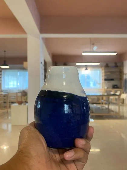 This is the result of patience, practice, and passion. A student's finished vase, glazed and fired, held up against the backdrop of the studio where it was made. Every piece that leaves our kiln tells a story of growth and the joy of creating something beautiful and functional with your own hands.