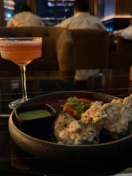 A close-up of the delicious malai tikka and a craft cocktail at Limitless Luxe, showcasing the quality of their food and drinks.