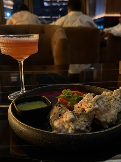 A close-up of the delicious malai tikka and a craft cocktail at Limitless Luxe, showcasing the quality of their food and drinks.