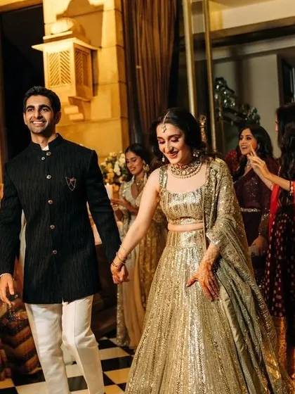 A perfect look for a sangeet or reception night. The groom looks sharp in a black striped bandhgala paired with white trousers, complementing his partner's shimmering gold lehenga for a glamorous and modern couple statement.