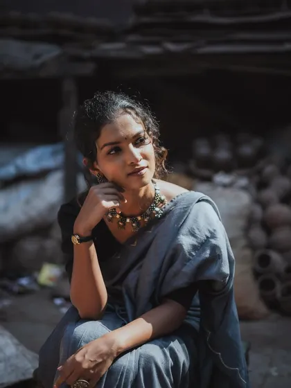 A candid, thoughtful portrait in a rustic setting. The model rests her chin on her hand, looking away with a pensive expression, all captured in beautiful, natural light.