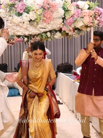 The bride's grand entrance under a beautiful floral canopy. Her entire look, from the golden saree to the elegant hair and makeup, is designed to make a statement.