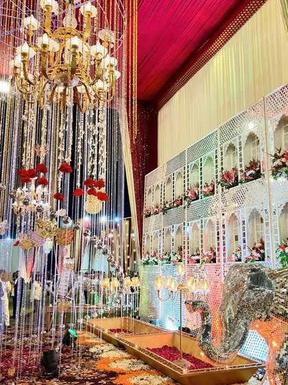 An opulent decor setup with a cascade of hanging crystals and flowers in front of a traditional Rajasthani jharokha wall.