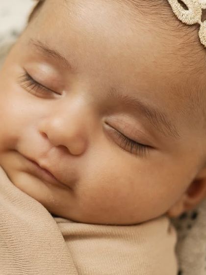 A close-up of a sleeping newborn's face, showing her long eyelashes and the sweet butterfly headband.