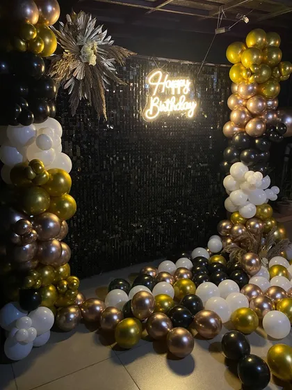 A glamorous birthday setup with a black shimmer wall and a balloon arrangement in black, white, gold, and rose gold.