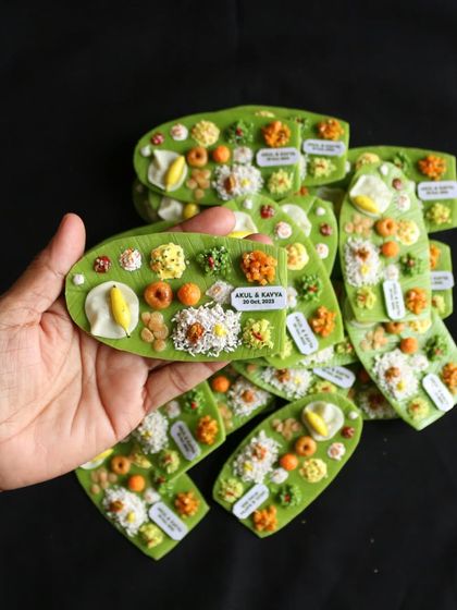 Holding a handful of personalized banana leaf magnets, a popular choice for wedding return gifts.