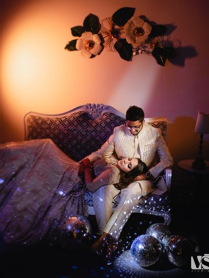 A unique, artistic portrait from Archana and Akhil's sangeet. The couple relaxes on a vintage sofa surrounded by disco balls, creating a scene that is glamorous, intimate, and full of cool, moody vibes.