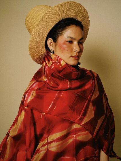 A studio portrait for House of Wandering Silk, combining a traditional hat with a modern, flowing garment. The look is both artistic and stylish.