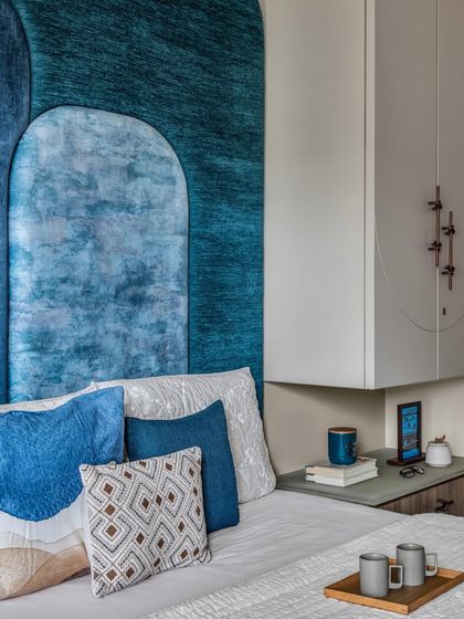 A close-up of the guest bedroom, showing the layered blue headboard and the custom floating wardrobe and mandir unit, designed to maximize space.