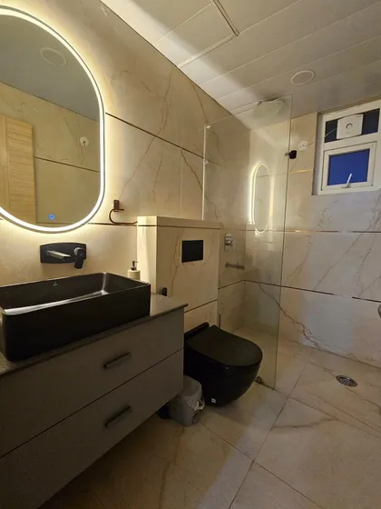 A minimalist and luxurious bathroom design with marble-patterned tiles, a black rectangular sink, and a sleek wall-mounted vanity. The backlit oval mirror adds a soft, ambient glow to the space.