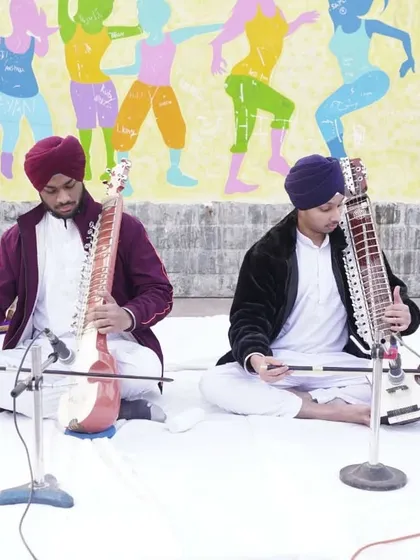 A duet performance featuring two different bowed string instruments, the Taus and the Dilruba, at an outdoor event.