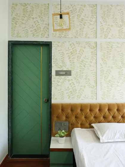 The combination of the patterned wallpaper, tufted headboard, and bold green door creates a layered and sophisticated look.