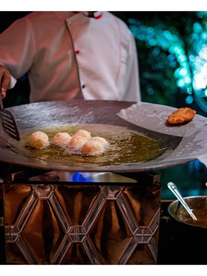 A chef deep fries savoury items in a large kadai. This traditional cooking method, performed live, brings authentic flavours and a touch of nostalgia to any Indian food station.