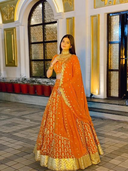 Full look of the orange Banarasi lehenga, showing its elegant fall and the matching gold jewellery.