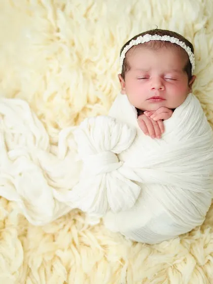 A full-length view of the newborn in the elegant white bow swaddle, creating a beautiful and classic portrait on the soft fur rug.