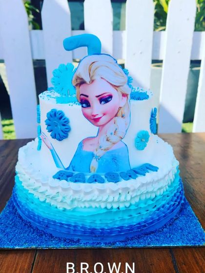 A two-tier Frozen cake with a dark blue ombre effect. This design is perfect for a winter-themed party, featuring Elsa and edible snowflakes.