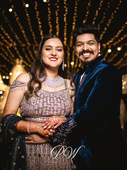 A happy couple portrait against a backdrop of fairy lights. The warm glow creates a romantic and intimate atmosphere for their Sangeet night.