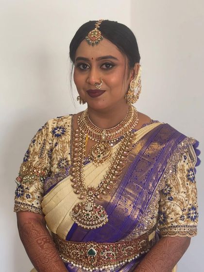 A beautiful bride in a traditional white and purple silk saree, with her hair neatly styled to complement her temple jewellery.