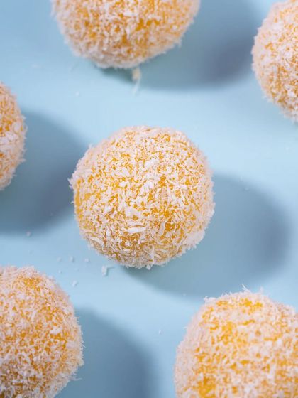 A flat lay of mango coconut laddoos against a solid blue background. This minimalist, colorful style is very effective for e-commerce and social media.