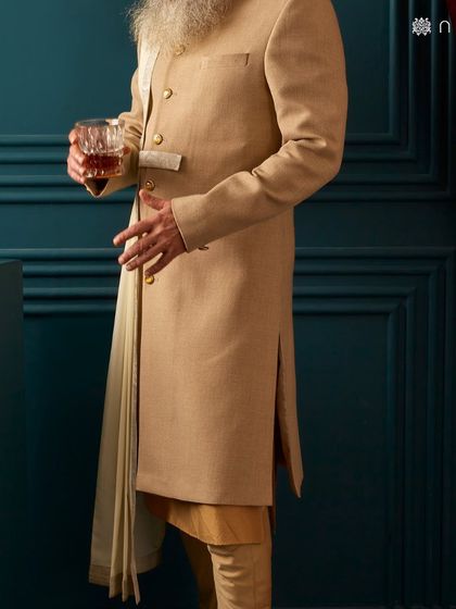 This beige sherwani with a unique draped panel offers a contemporary twist on a classic silhouette. It’s an architectural and sophisticated choice for the modern groom.