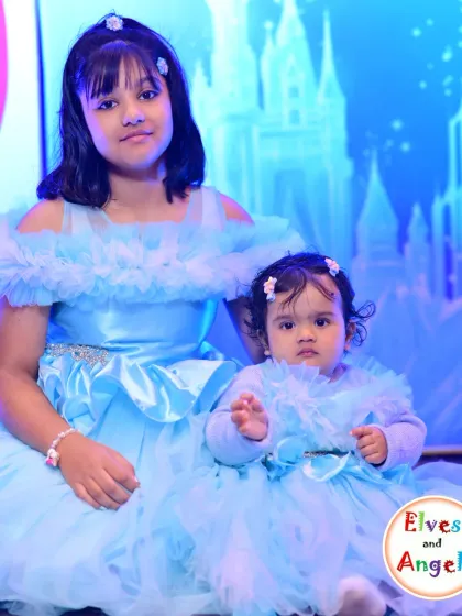 The birthday girls at the Frozen party, dressed in matching blue gowns in front of the ice castle backdrop. These are the moments I love to help create.
