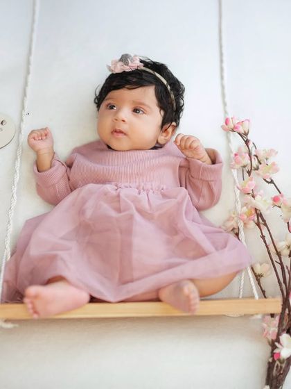 A lovely portrait of a baby girl on a cherry blossom swing for her three-month photoshoot. The setup is simple and sweet, perfect for this age.