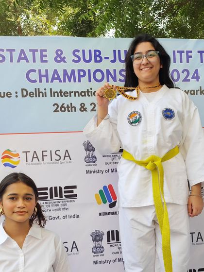 A yellow-belt student beams with pride as she shows off her gold medal.