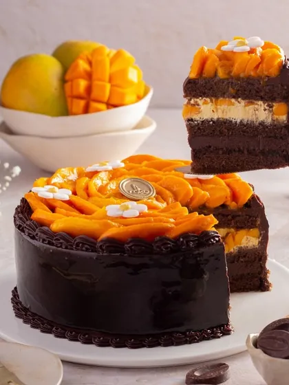 A slice of our Chocolate Mango Cake being lifted from the whole cake, showcasing its moist crumb and layers of mango cream. It's a tempting preview of this unique seasonal dessert.
