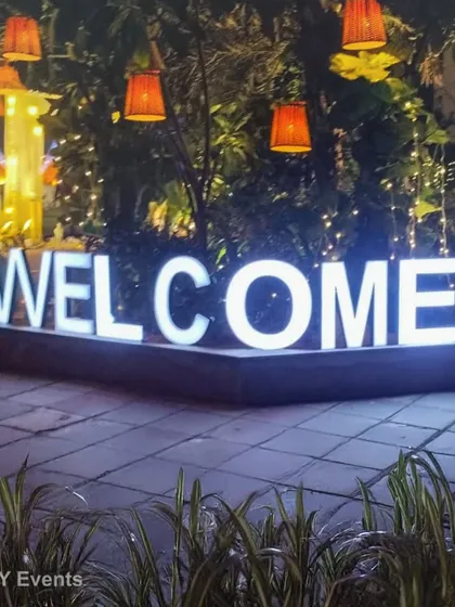 A simple yet effective illuminated "WELCOME" sign set amidst greenery. This is a classic and warm way to greet guests at any corporate conference, seminar, or evening function.