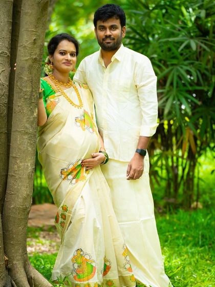 A traditional couple's portrait in a natural setting. Dressed in classic South Indian attire, they stand by a tree, blending cultural heritage with the beauty of the outdoors.