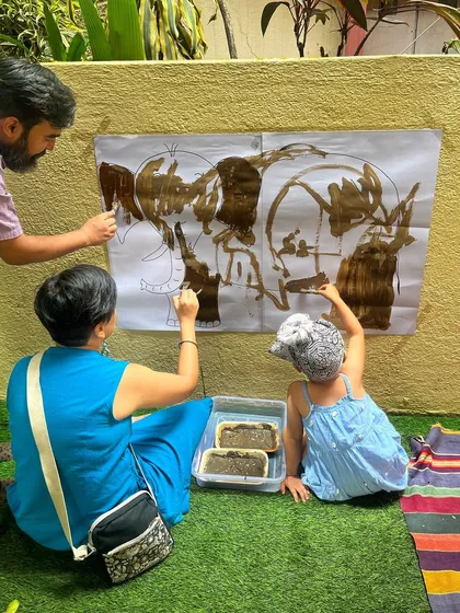I believe play is a powerful way for families to connect. Here, parents and a child work together on a large-scale mud painting, turning a simple art activity into a memorable bonding experience.
