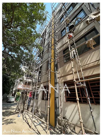 Construction of the side facade of the Yellow Line Apartment. The yellow-painted boxing for the plumbing pipes is visible, showing how a functional element was integrated into the design.