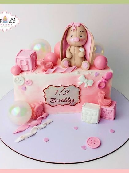 A sweet and simple half-birthday cake, decorated with a cute bunny, baby blocks, and buttons in shades of pink.