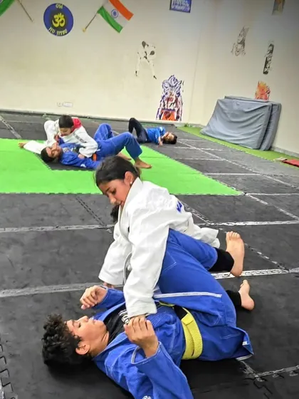 A lot of real-world situations end up on the ground. We teach Brazilian Jiu-Jitsu so kids learn to use leverage and control, not just strength. This picture shows a focused grappling session where students practice holds and positions in their Gi uniforms.