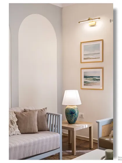 A corner of the coastal-themed living room, featuring an arched wall niche and framed watercolor prints of the sea. The soft lighting and natural textures create a calm and serene atmosphere.