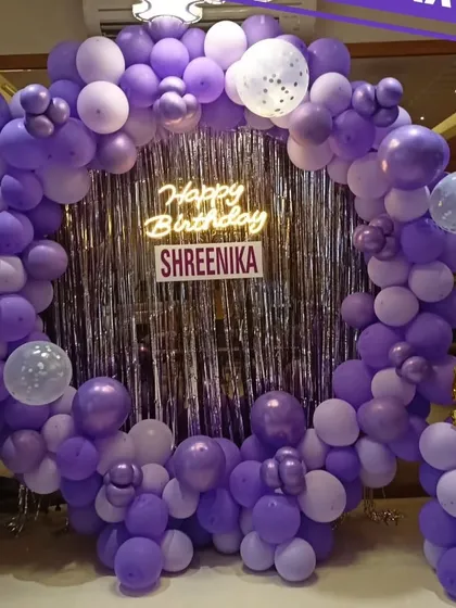A beautiful purple-themed birthday party with a full circular balloon arch, a silver sequin backdrop, and a neon sign for Shreenika's celebration.