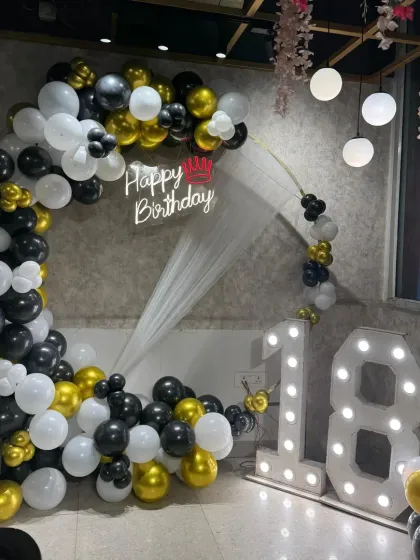 An 18th birthday party with a black, white, and gold balloon ring, a neon sign, and large marquee numbers.
