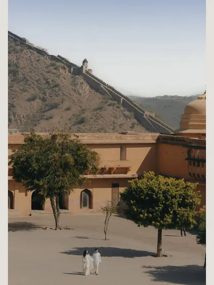 A wide-angle shot capturing the scale of Amer Fort's walls in Jaipur. Placing the couple in this vast landscape tells a story of a grand journey together.