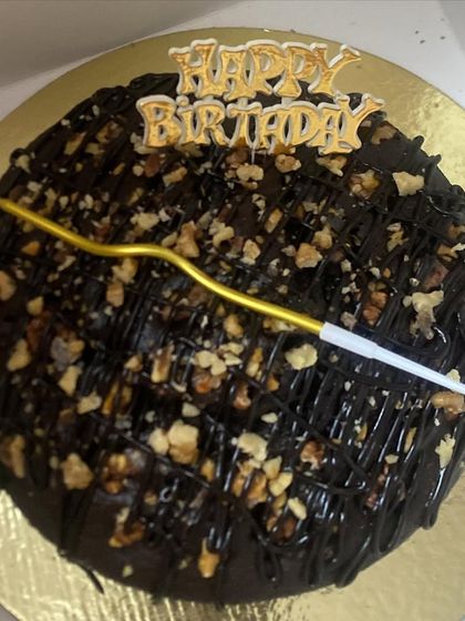 A classic chocolate tea cake decorated for a birthday celebration. It's topped with chopped walnuts, a chocolate drizzle, and a "Happy Birthday" pick, making it a simple yet elegant choice.