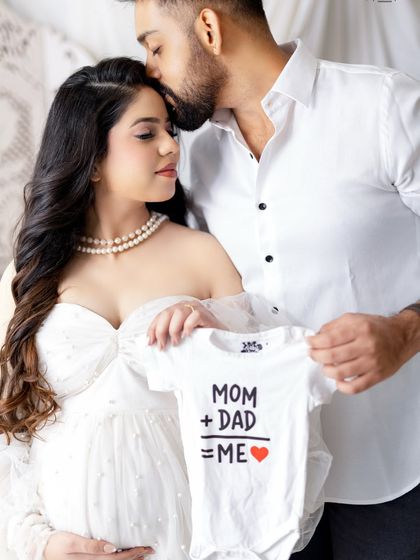 A cute and modern way to announce your pregnancy. Using props like this "Mom + Dad = Me" onesie adds a playful and personal element to your photos.