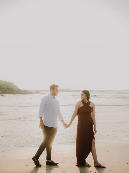 A wide shot of the couple holding hands on the beach. The vastness of the sea and sky creates a beautiful, serene backdrop for their pre-wedding portrait.