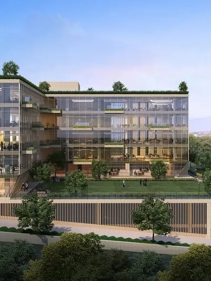 A different perspective of the commercial building in Navi Mumbai, showing its L-shaped form and the integration of green lawn spaces. The transparent glass façade allows for ample natural light, creating a bright and productive work environment.